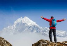 Hiker with arms raised facing snowy mountain peak