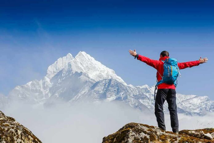 Hiker with arms raised facing snowy mountain peak