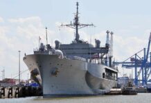 Large gray naval ship docked at an industrial port