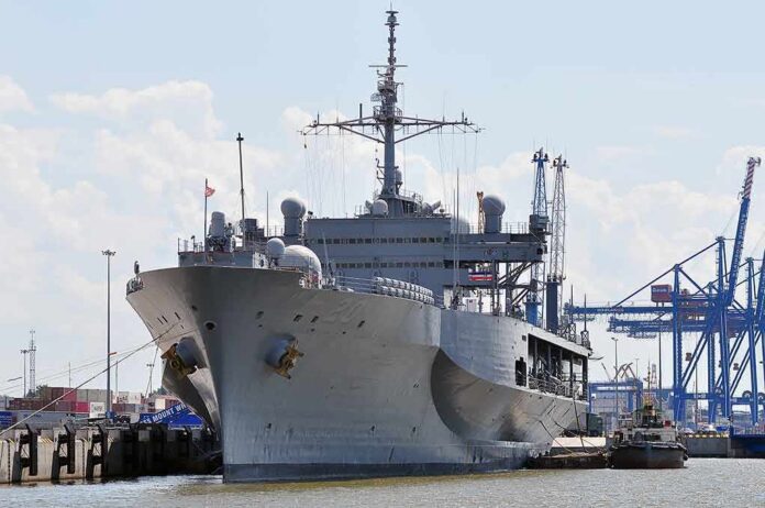 Large gray naval ship docked at an industrial port