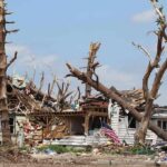 Storm-damaged house with fallen trees and debris