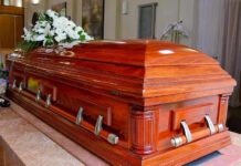 Three Suspects Captured After Church Massacre Wooden casket with white flowers in a funeral home.