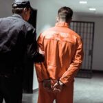 Goat Head Ultimatum After Kingpin Grab Police officer escorting handcuffed inmate in orange jumpsuit