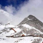 Snow-covered mountain with hiking trails and tourists under a cloudy sky