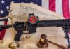 Rifle with NRA badge on Constitution backdrop with scales and gavel