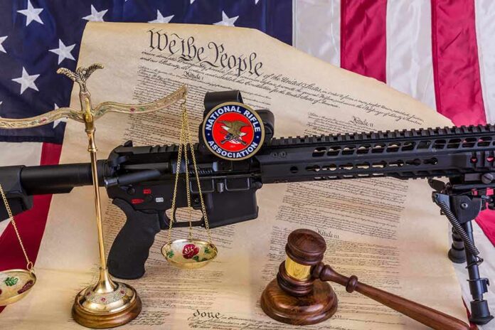 shutterstock_1089834179 Rifle with NRA badge on Constitution backdrop with scales and gavel