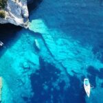 Aerial view of boats in turquoise coastal waters near a sea cave
