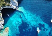 Aerial view of boats in turquoise coastal waters near a sea cave