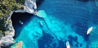 Aerial view of boats in turquoise coastal waters near a sea cave