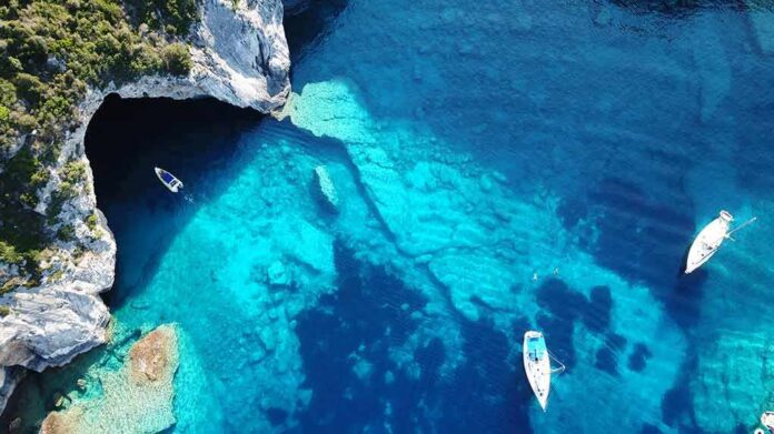 Aerial view of boats in turquoise coastal waters near a sea cave
