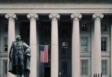 Statue in front of a neoclassical government building with columns and a U.S. flag