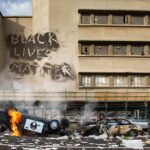 Burning overturned police car in front of a damaged building