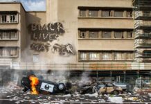 Burning overturned police car in front of a damaged building