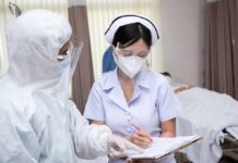 Lab Worker Dies as Plague Fears Trigger Quarantine nurse in PPE writing on a clipboard with colleague