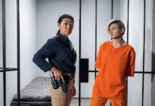 Police officer stands beside inmate in orange uniform inside a jail cell