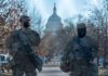 Two armed soldiers stand guard near a domed government building