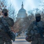 Two armed soldiers stand guard near a domed government building