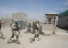 Soldiers in desert uniforms run past a checkpoint amid dust