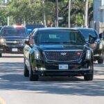 Motorcade of black SUVs and sedans driving down a city street