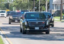 Motorcade of black SUVs and sedans driving down a city street