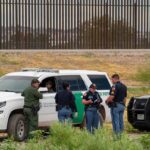 Maritime Crackdown Exposes Chilling Trend law enforcement officers confer beside patrol vehicles near a border fence