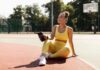 Woman in yellow activewear sitting on outdoor court with water bottle