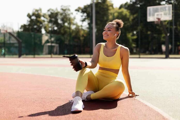 shutterstock_2029452341 Woman in yellow activewear sitting on outdoor court with water bottle
