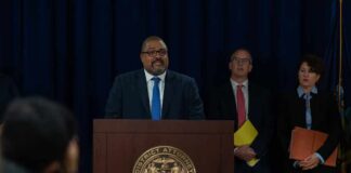 Man at podium during press conference with officials behind him
