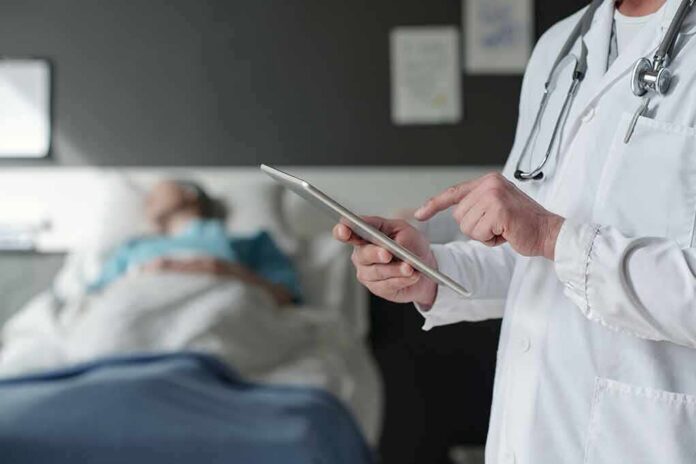 shutterstock_2316812635-1 Doctor using tablet beside hospital patient