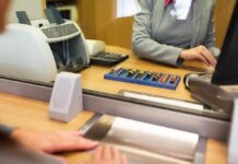 Brink’s Blunder: $128K Left On ATM Bank teller at counter handling cash and coins
