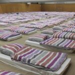 Gym Coach’s Double Life – Judge Drops Hammer rows of mattresses with striped bedding in a large hall