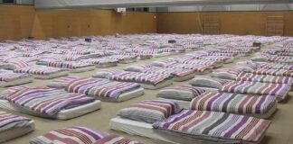 rows of mattresses with striped bedding in a large hall