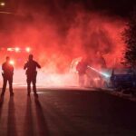 Halloween Celebration Erupts in Gunfire Police officers watch firefighters extinguish a car fire at night