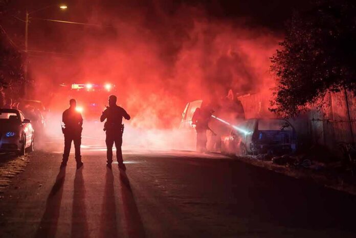 shutterstock_680426953 Police officers watch firefighters extinguish a car fire at night