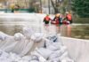 Flood Rescue: Reporter Makes Split-Second Leap Sandbags stacked near a flooded street with rescue workers in a boat