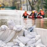 Flood Rescue: Reporter Makes Split-Second Leap Sandbags stacked near a flooded street with rescue workers in a boat